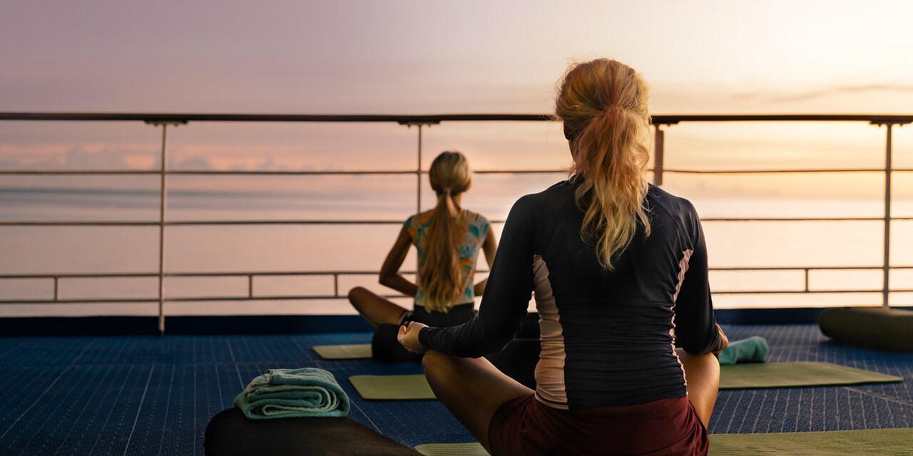 Two woman in yoga poses on a ship’s deck looking out over the sea
