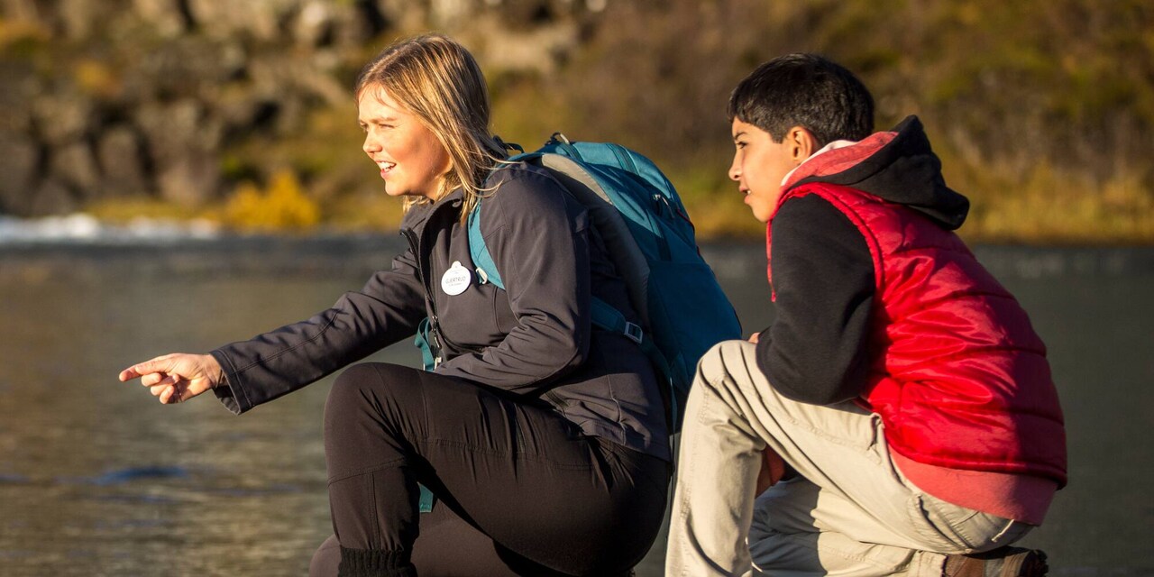 An Adventure Guide and a boy squatting on a rocky surface, looking at a site in the distance An Adventure Guide and a boy squatting on a rocky surface, looking at a site in the distance