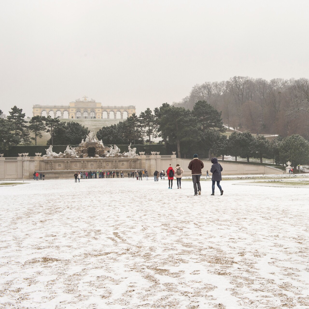 Groups of people walk along a snowy path towards Neptune Fountain at the foot of Schönbrunn Palace