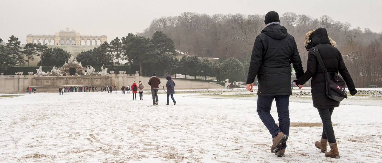 Groups of people walk along a snowy path towards Neptune Fountain at the foot of Schönbrunn Palace