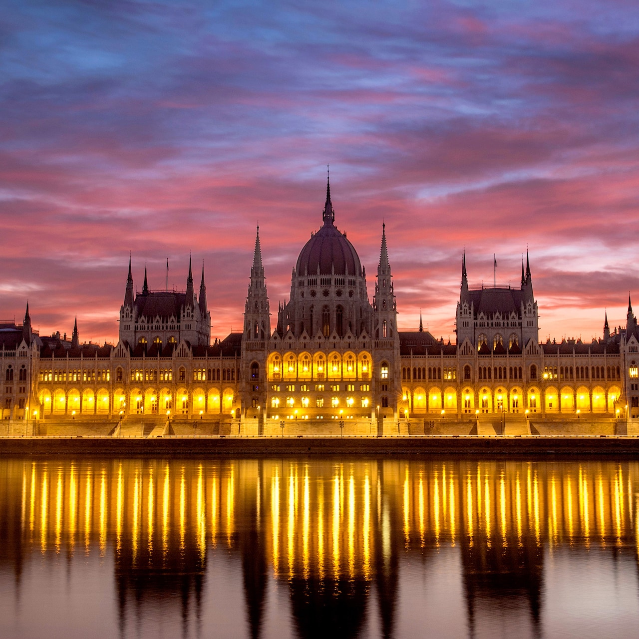 The Budapest Parliament building at sunset, with reflections of its lights on the Danube River The Budapest Parliament building at sunset, with reflections of its lights on the Danube River