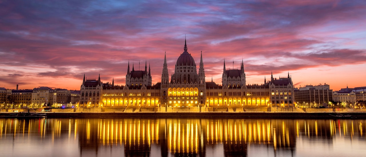 The Budapest Parliament building at sunset, with reflections of its lights on the Danube River The Budapest Parliament building at sunset, with reflections of its lights on the Danube River