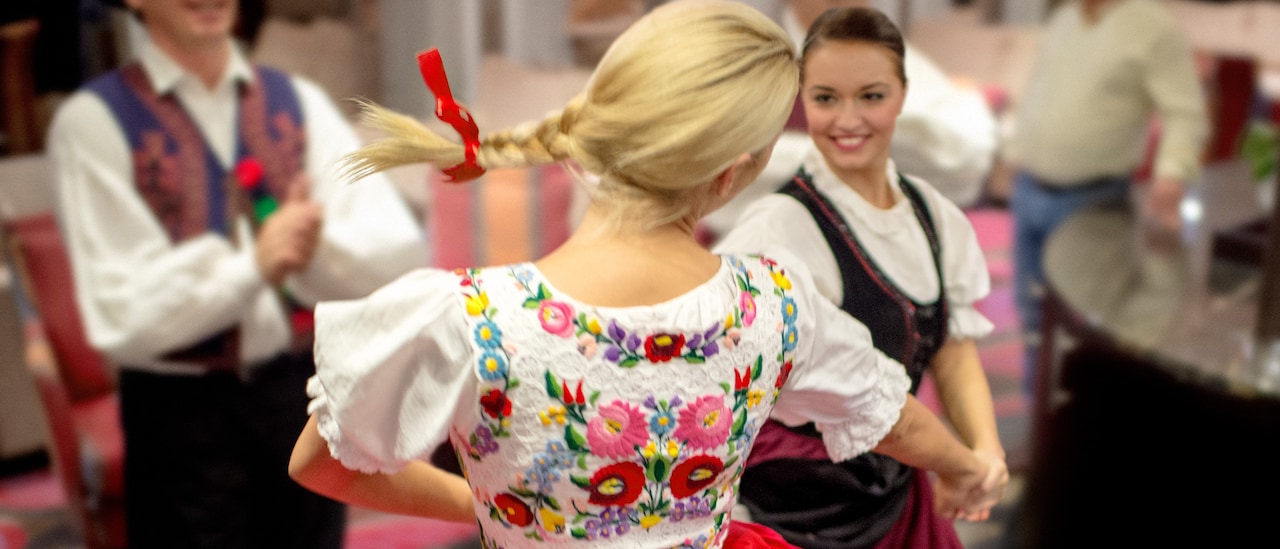 2 women wearing traditional costumes dance as a costumed male dancer claps 2 women wearing traditional costumes dance as a costumed male dancer claps