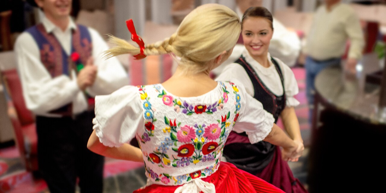 2 women wearing traditional costumes dance as a costumed male dancer claps 2 women wearing traditional costumes dance as a costumed male dancer claps
