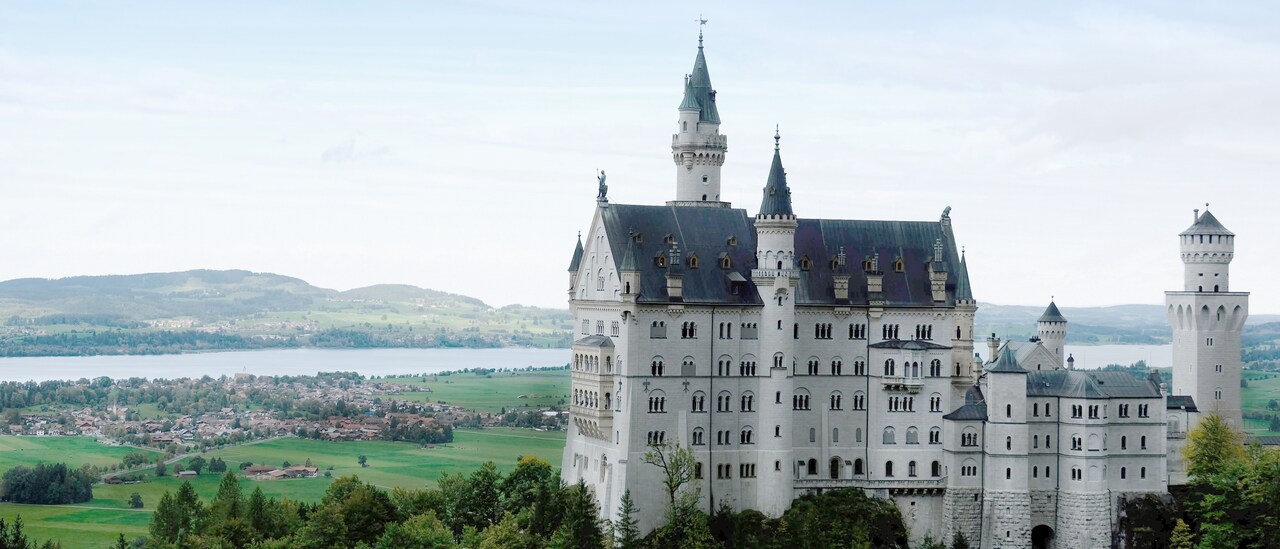 Neuschwanstein Castle stands on a hilltop above a town in the valley below on the banks of a river