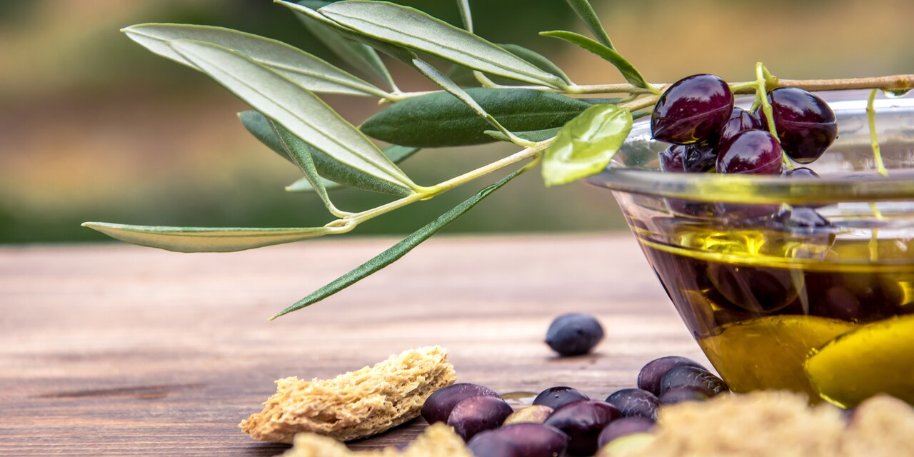An olive branch rests on a glass bowl of olive oil