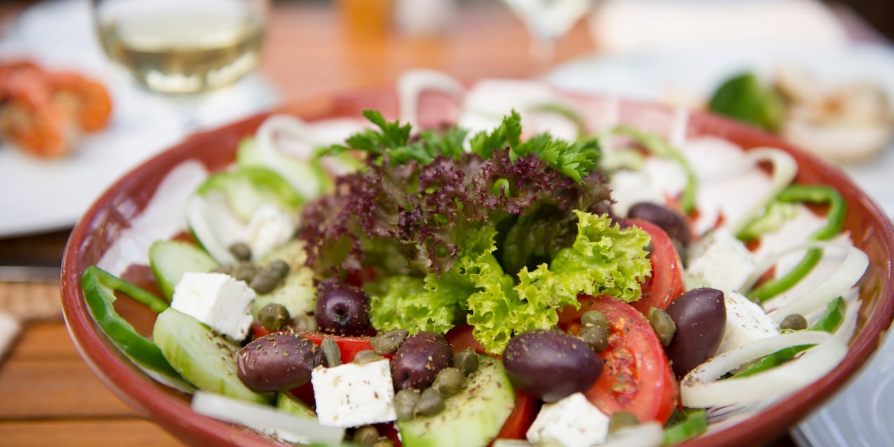 A Greek salad of onions, olives, tomato, lettuce and feta cheese is artistically arranged in a bowl