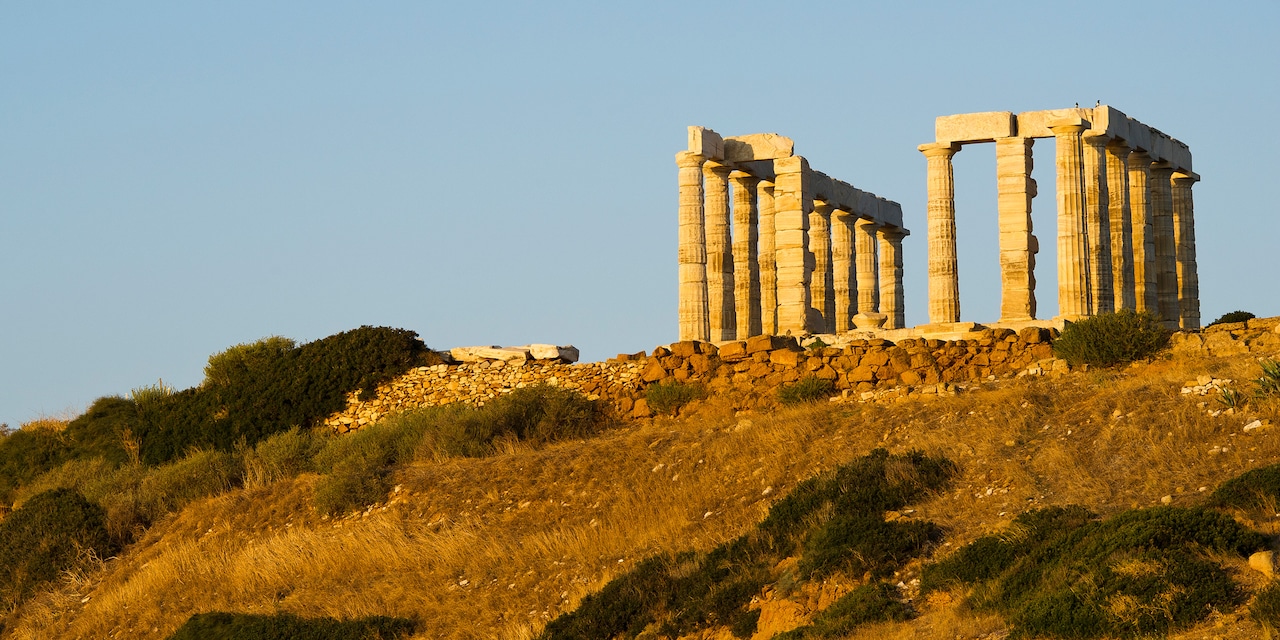 Two rows of upright columns stand among the ruins of the Temple of Poseidon atop a hill beneath a clear sky