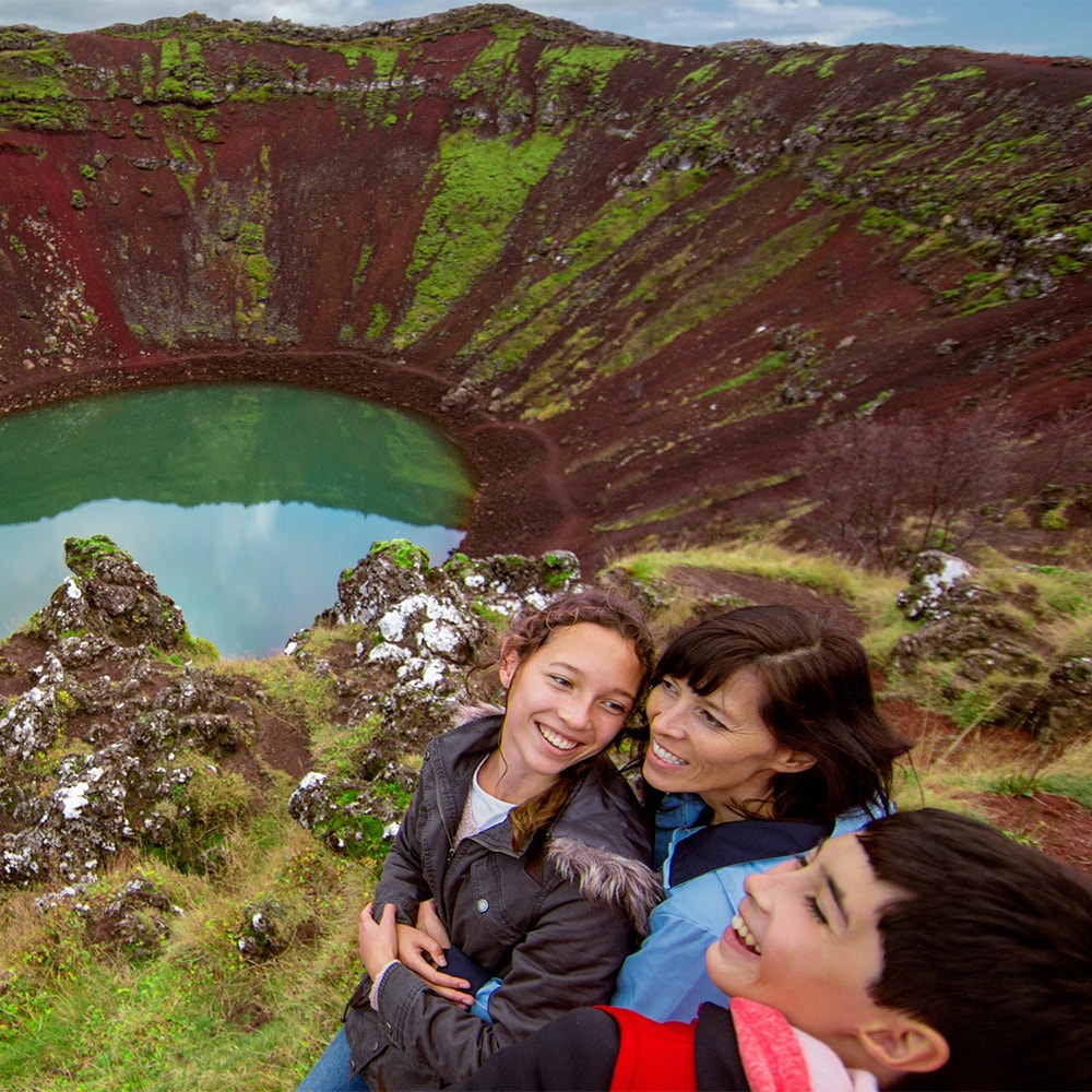 3 people sit on a bench near the water in Kerið Crater