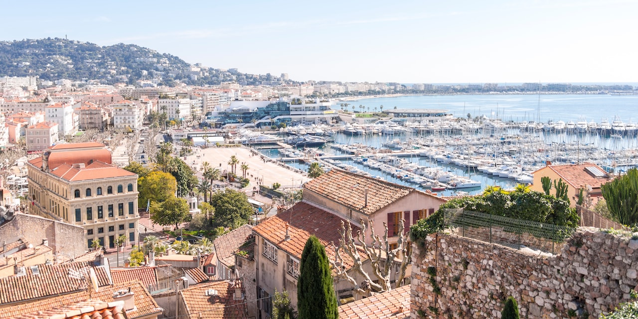 Boats docked in the Cannes Harbor, with multi storied, tile roof buildings hugging the shore Boats docked in the Cannes Harbor, with multi storied, tile roof buildings hugging the shore