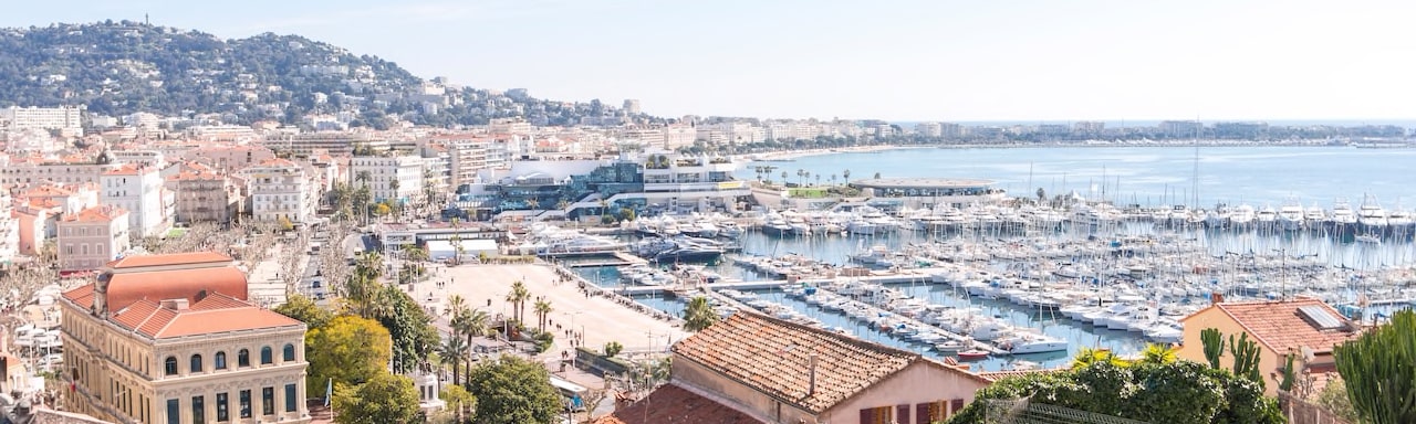 Boats docked in the Cannes Harbor, with multi storied, tile roof buildings hugging the shore Boats docked in the Cannes Harbor, with multi storied, tile roof buildings hugging the shore