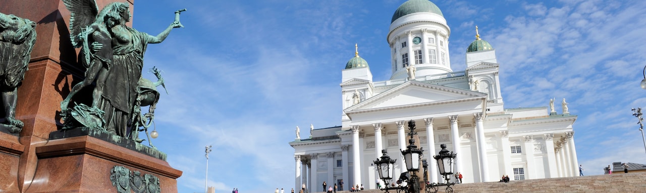 A statue of an angel at the bottom of stairs leading to a building with pillars and 3 domes A statue of an angel at the bottom of stairs leading to a building with pillars and 3 domes