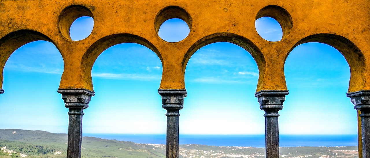 An archway with circular patterns with a view of the ocean in the distance