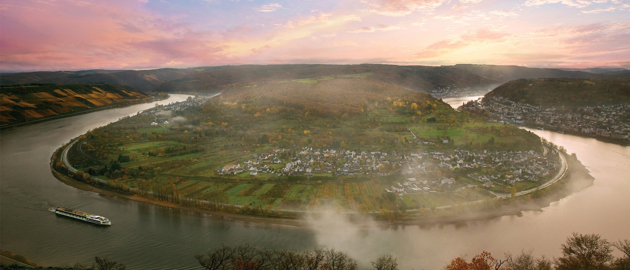 A horseshoe bend along the Rhine River with a town and lush landscapes surrounding an inner island