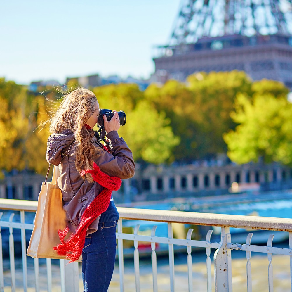 A woman with an SLR camera captures an image of the Eiffel Tower in the distance
