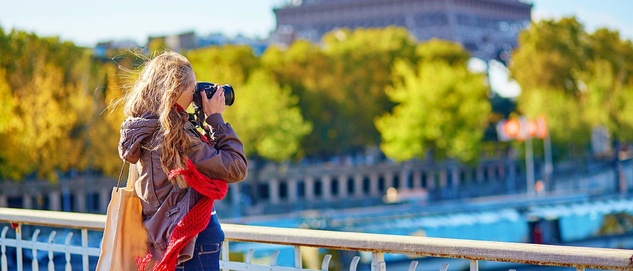 A woman with an SLR camera captures an image of the Eiffel Tower in the distance
