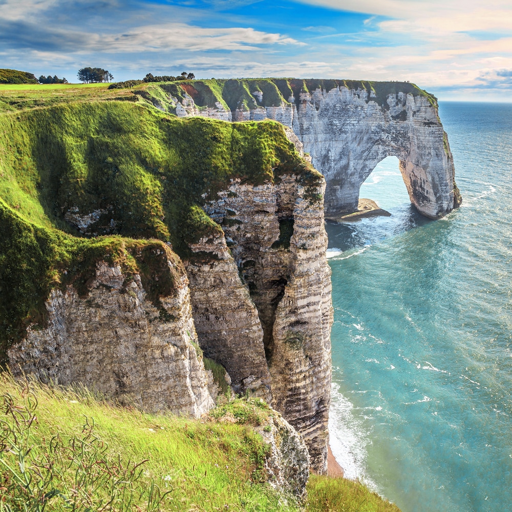 Grass covered cliffs with an arch-shaped structure rise high above the water