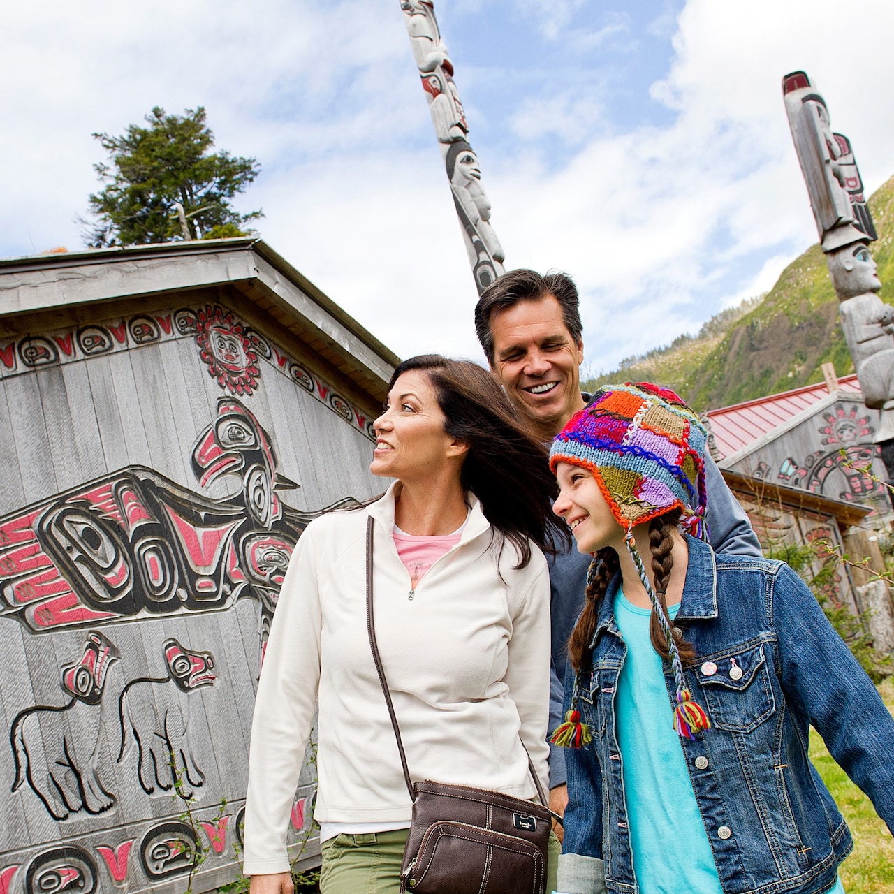 Mom, dad and daughter view an outdoor exhibit of native Alaskan artwork and totem poles ...