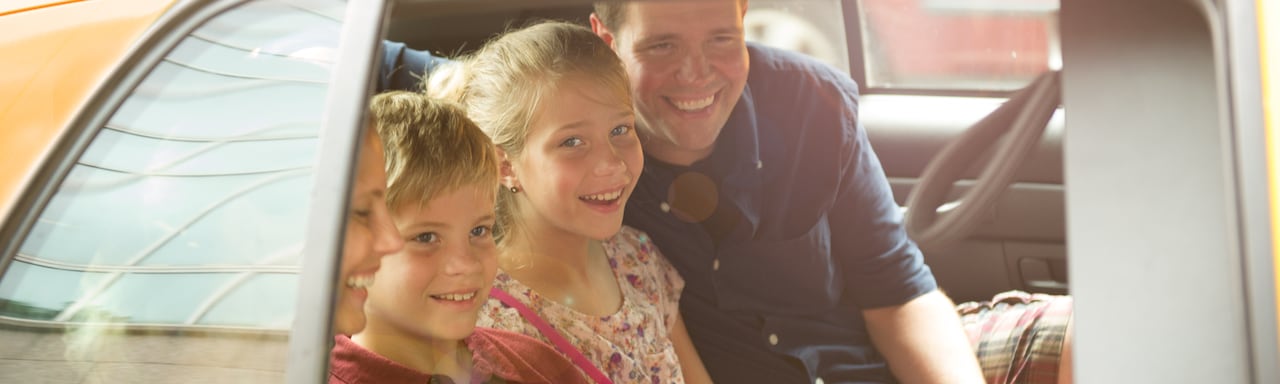 A smiling family of 4 rides in the back seat of a sedan A smiling family of 4 rides in the back seat of a sedan