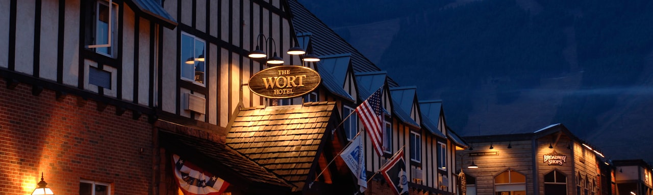 At night, a lit sign above the entrance to a building made of wood and brick reads 'The Wort Hotel'