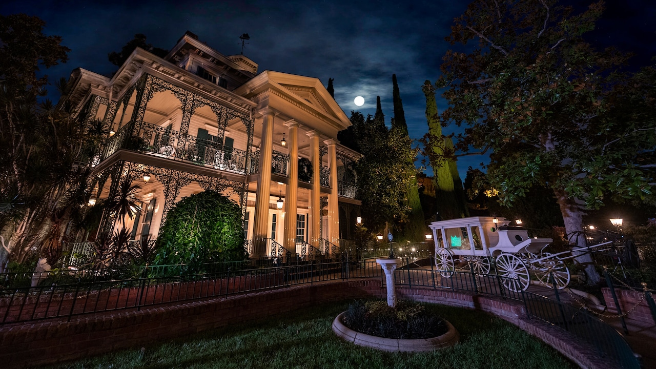 At nighttime, a horse drawn carriage sits outside the Haunted Mansion at Disneyland Park in California
