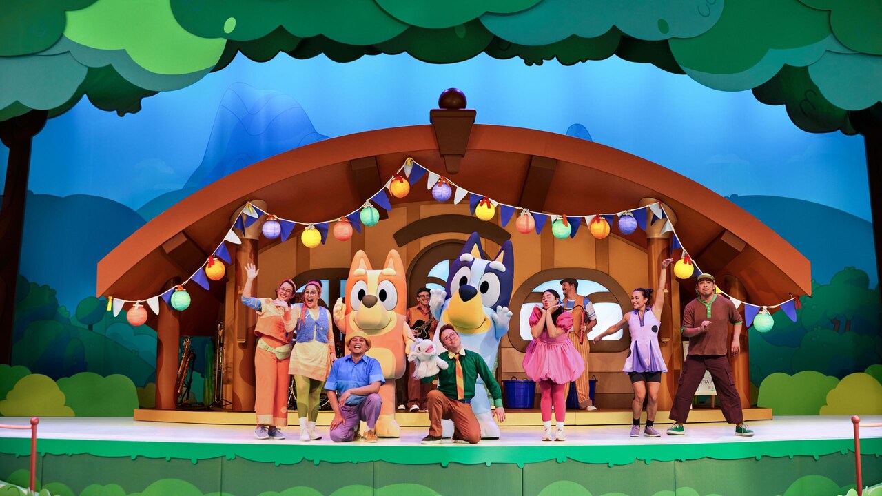 The cast of Bluey's Best Day Ever pose on a stage set designed to look like a house in the woods
