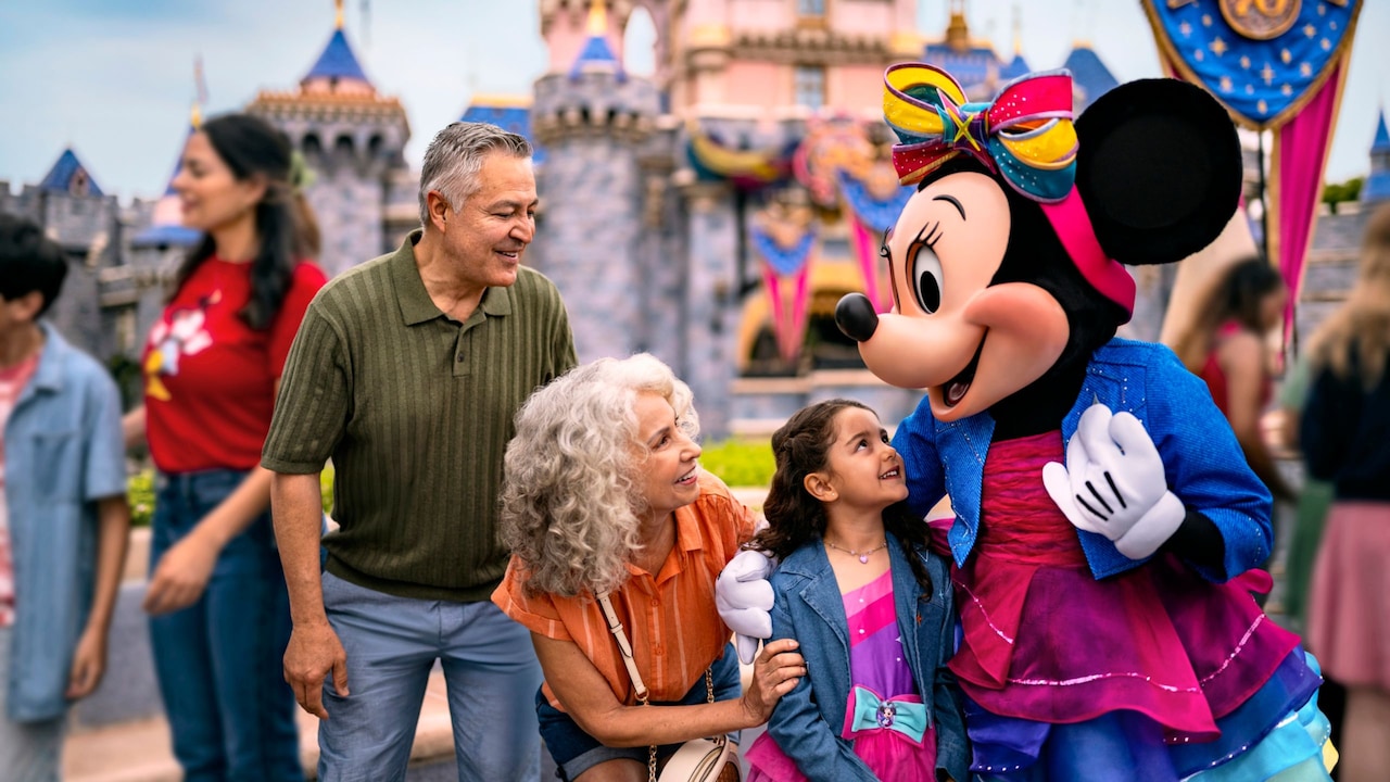 Minnie Mouse embracing a young girl next to her grandparents in front of Sleeping Beauty Castle