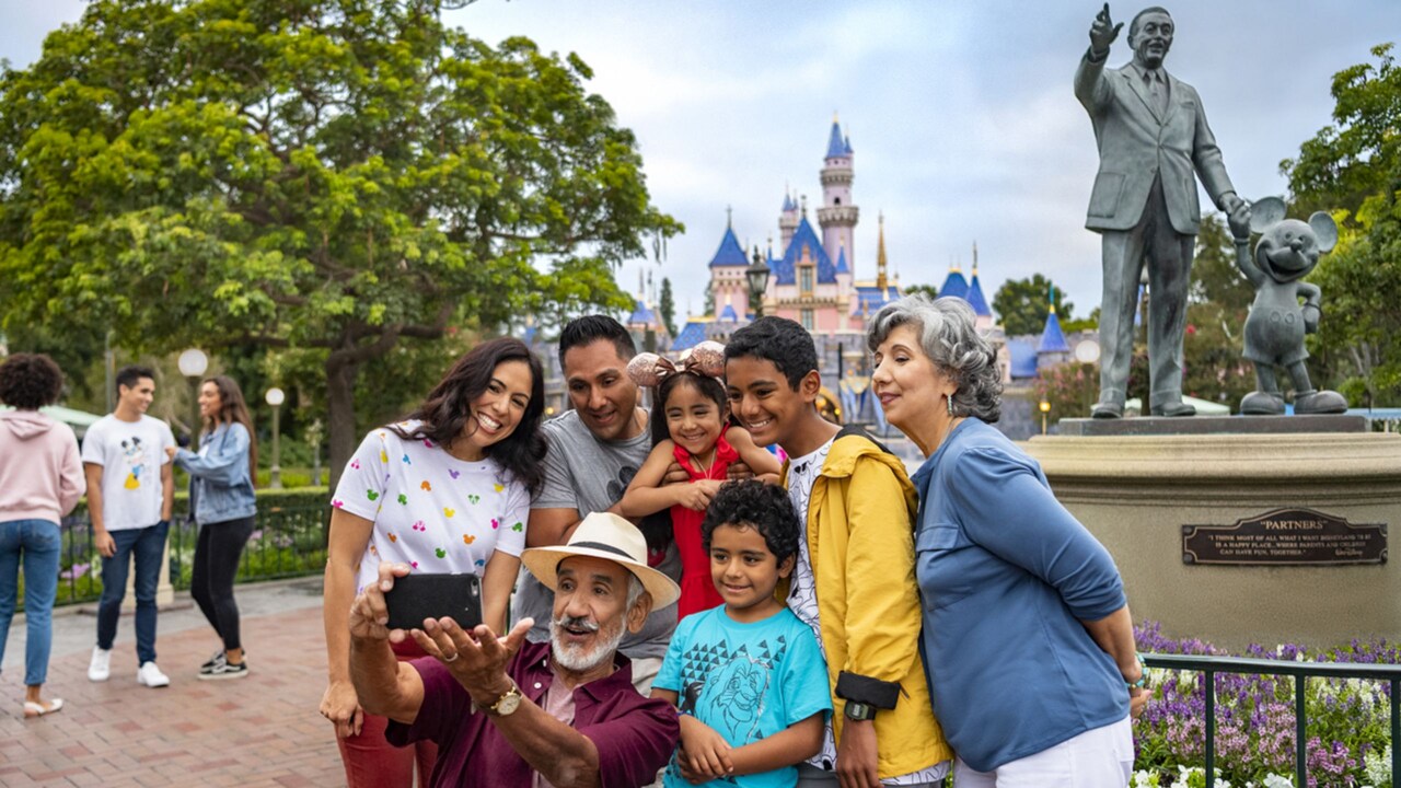 With Sleeping Beauty Castle in the background, a family poses for a picture by a statue of Mickey Mouse and Walt at the Disneyland Resort