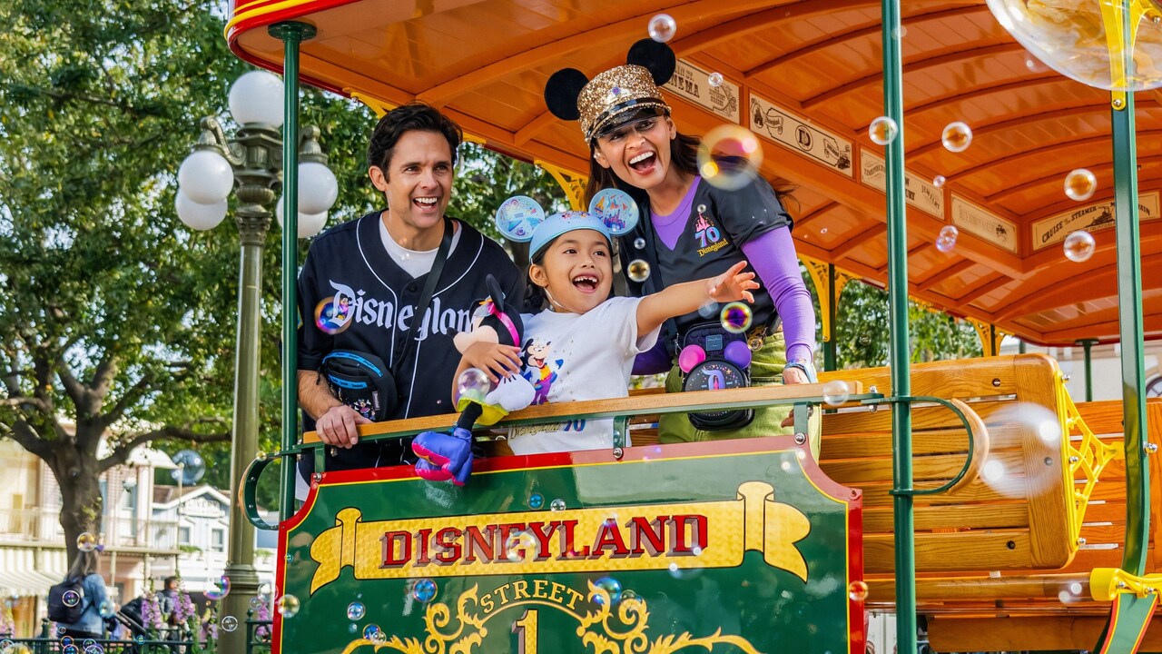 Dos padres y su hija con prendas de la Celebración del 70.º Aniversario del Disneyland Resort en un tranvía tirado por caballos