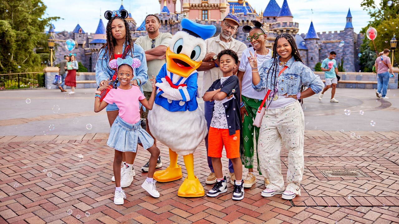 A family poses with Donald Duck in front of Sleeping Beauty Castle
