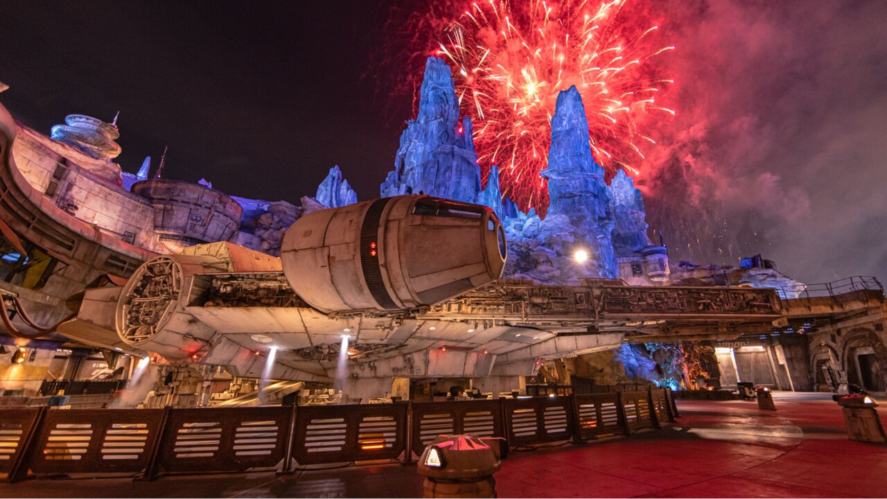 The Millennium Falcon docked in Star Wars Galaxy’s Edge at night with fireworks lighting up the sky