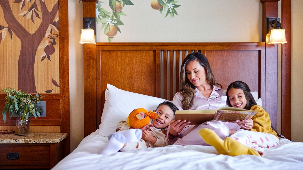 Una mamá les lee un cuento antes de dormir a sus hijos en una habitación de hotel de Disneyland Resort