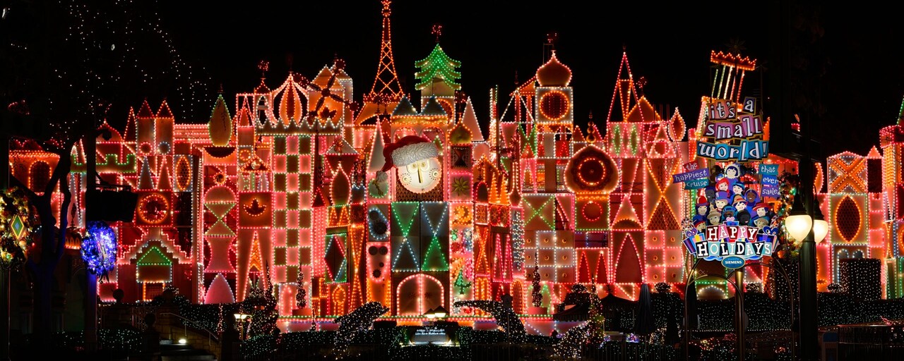 The façade of it’s a small world holiday at night with signs reading ‘it’s a small world and happy holidays’ and an illustration of children