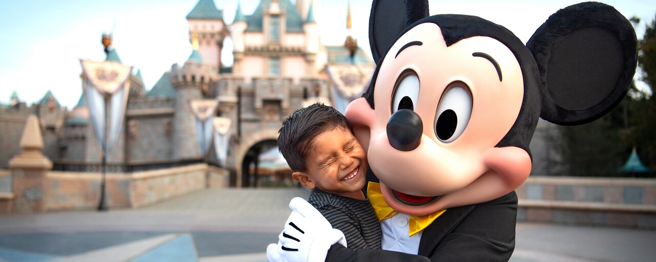 Mickey Mouse comparte un abrazo con un pequeño feliz invitado frente al Castillo de la Bella Durmiente