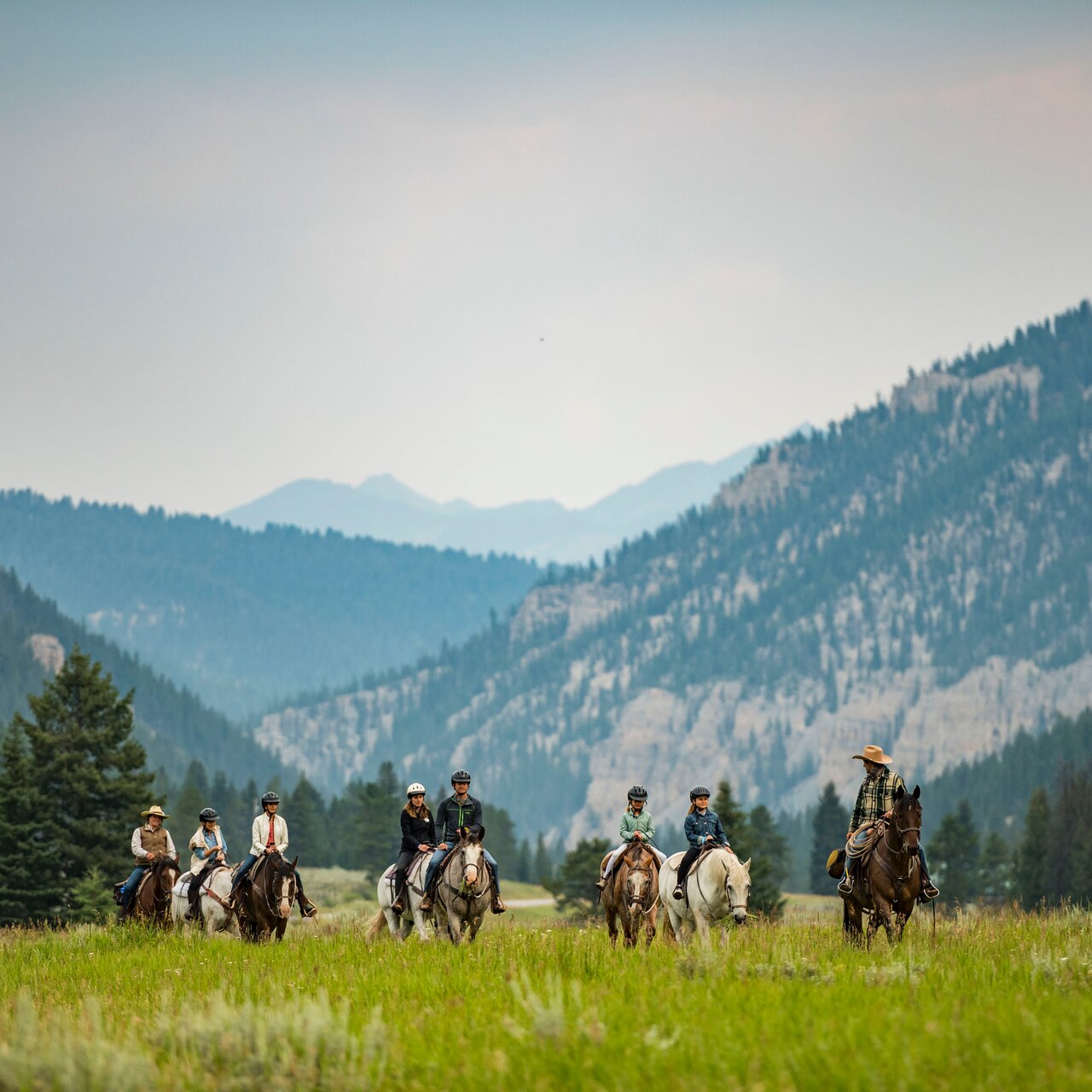 A group of people ride horses on the grassy plain of a mountain valley