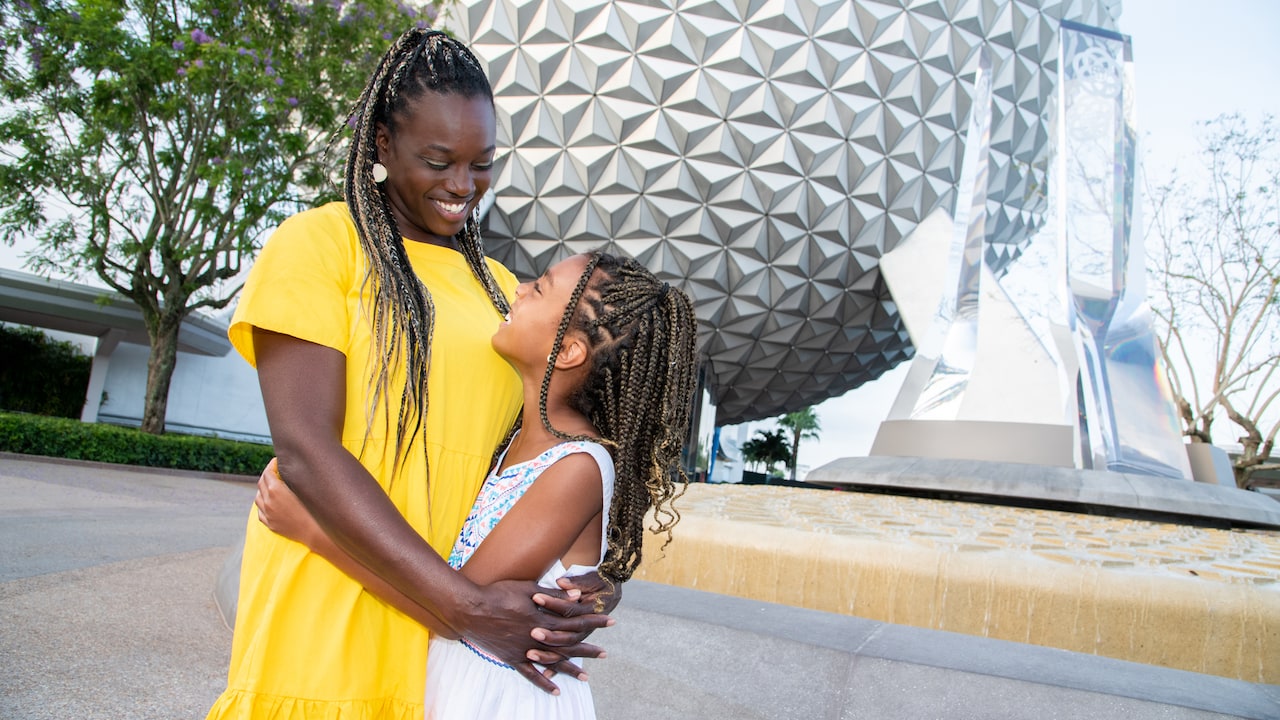 A mom and her daughter hug in front of Spaceship Earth