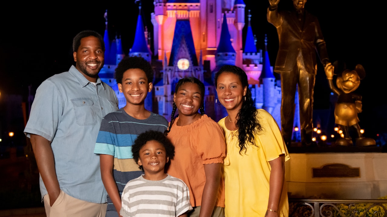 A family of 5 pose for a photo next to the Partners Statue and Cinderella Castle