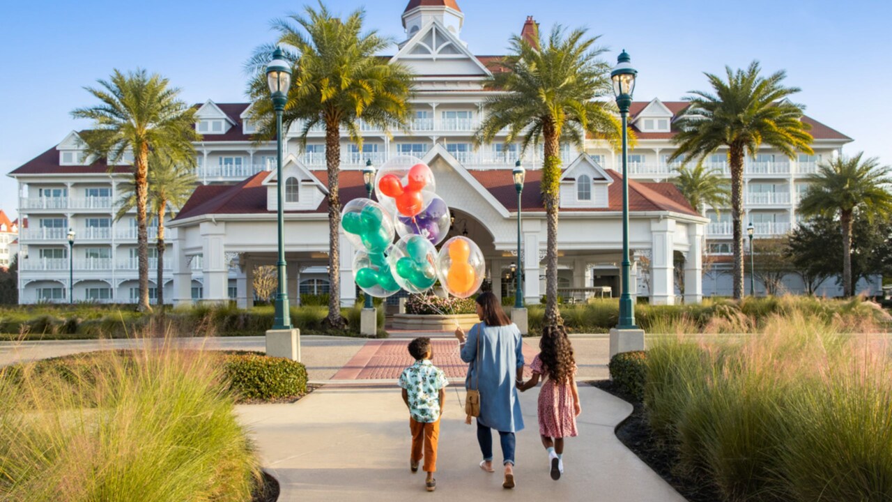 Woman holding Mickey balloons walks with her daughter and son into the entrance of Disney’s Grand Floridian Resort and Spa