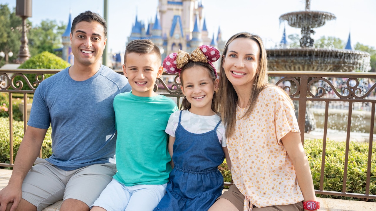 A family of 4 posing for a picture with Cinderella’s Castle at Magic Kingdom park in the distance