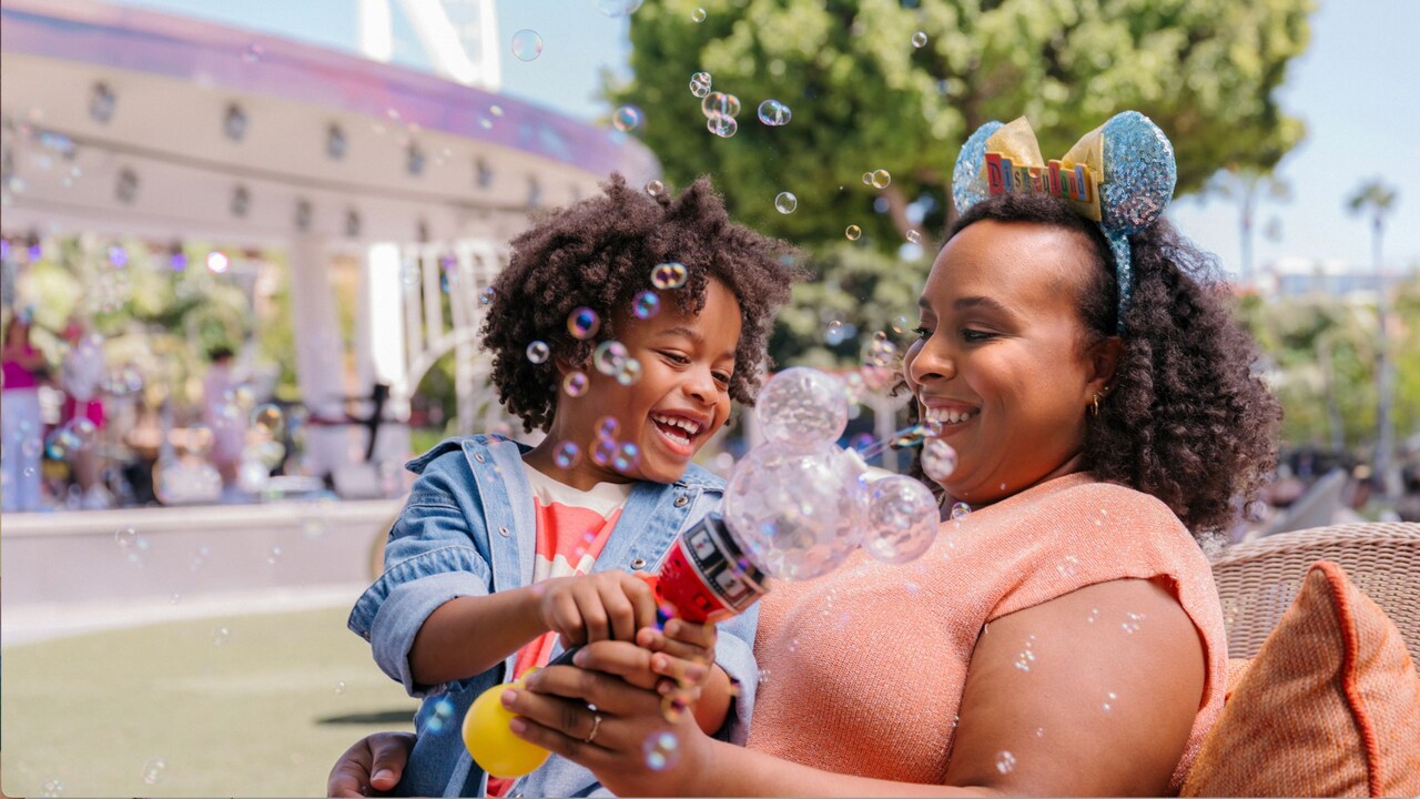 Una madre y su hijo jugando con una varita de burbujas de Mickey Mouse junto a Downtown Disney Live Stage