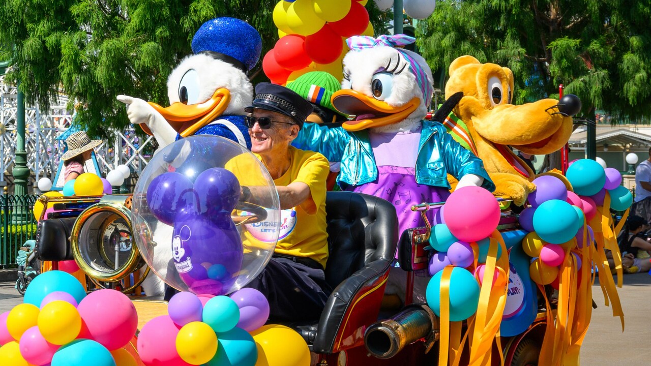 Donald Duck, Daisy Duck and Pluto riding a festive balloon covered vintage car during a parade 