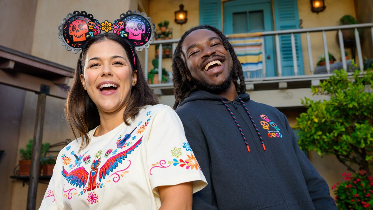 Dos Visitantes con prendas con temática de Coco, incluida una sudadera, una playera y una diadema con orejas de Minnie Mouse