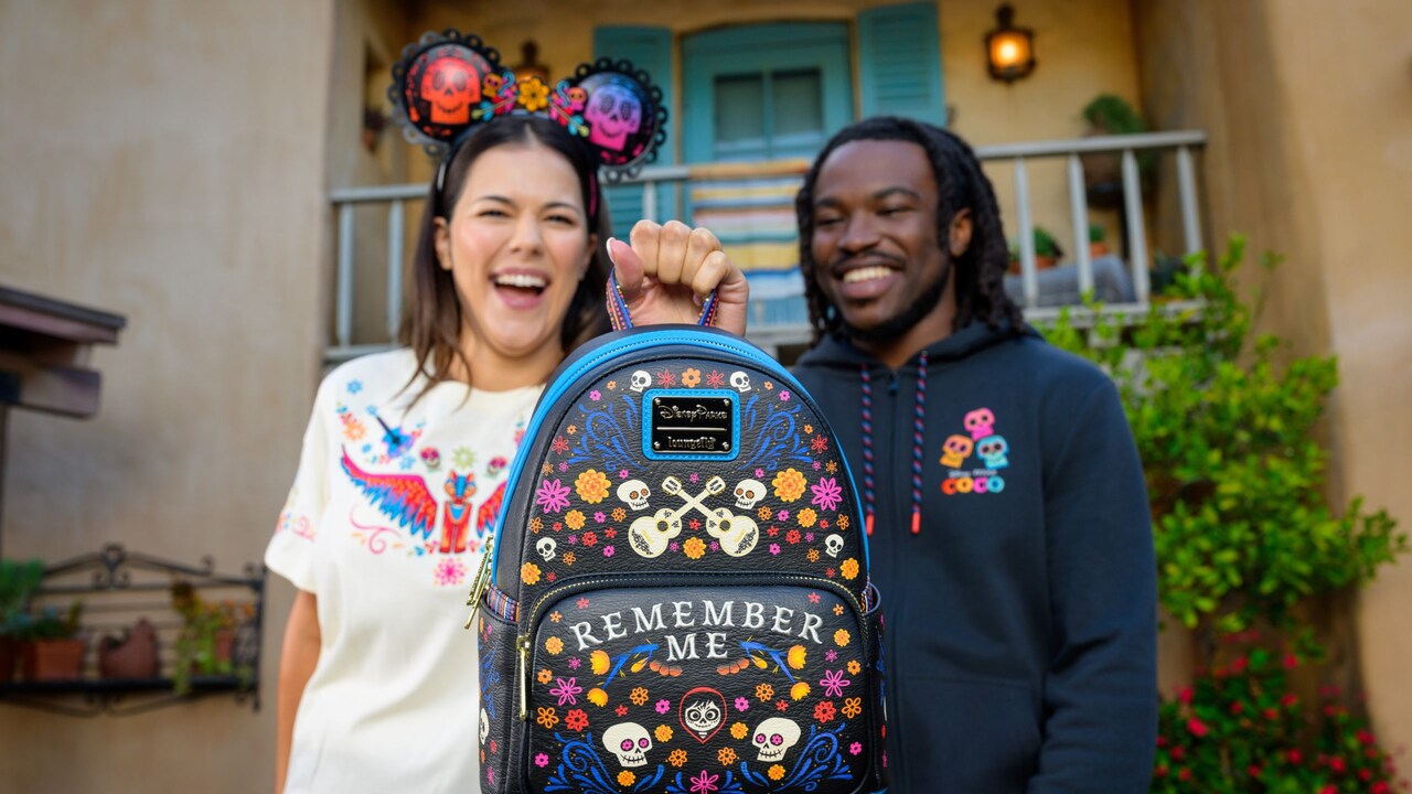 Dos Visitantes con una sudadera con capucha, una playera y una diadema de Minnie Mouse con temática de Coco sosteniendo una mochila Loungefly con temática de Coco