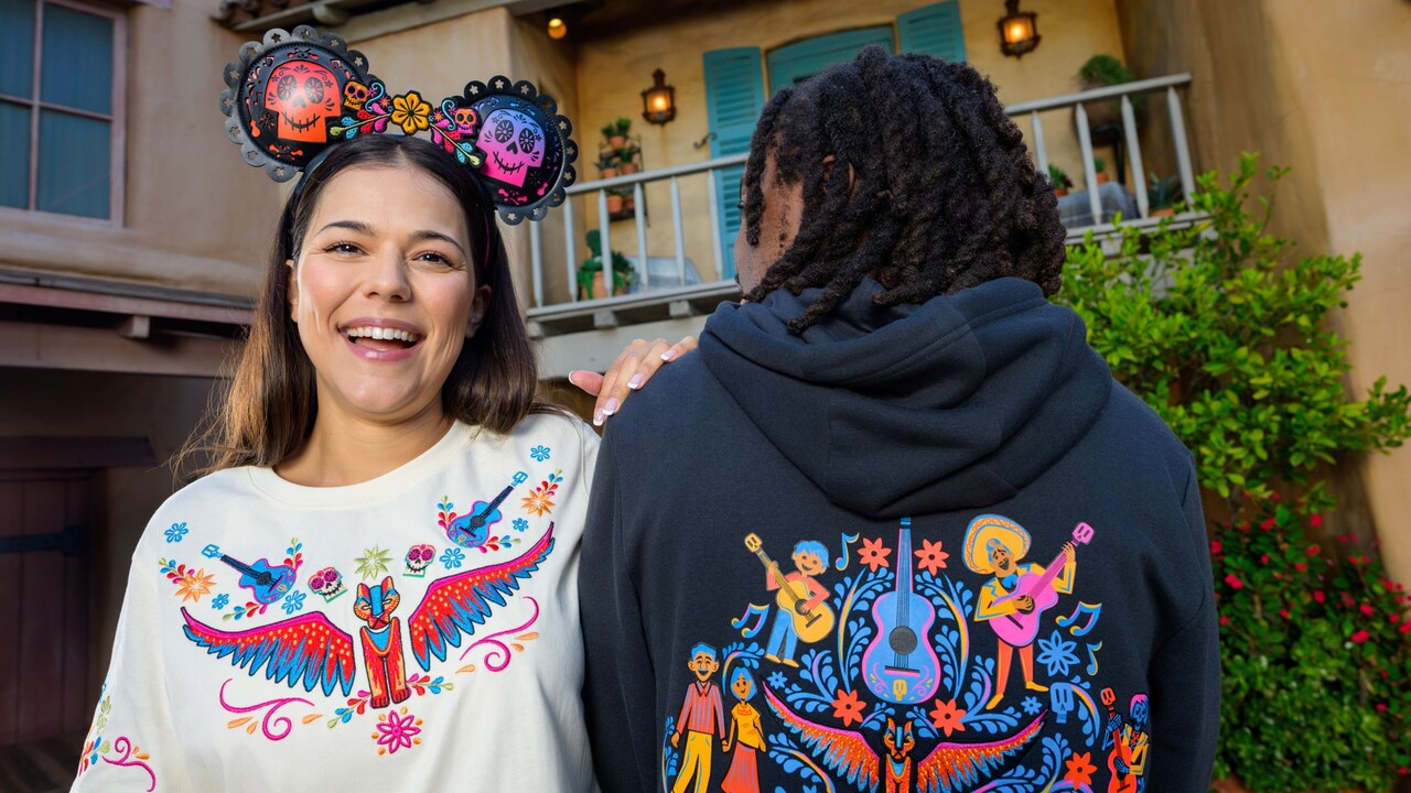 Dos Visitantes con una sudadera con capucha, una playera y una diadema de Minnie Mouse con temática de Coco