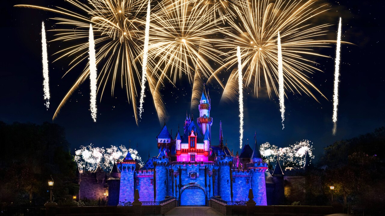 Una multitud de personas se reúne en Main Street U.S.A. mientras los fuegos artificiales explotan sobre el Castillo de la Bella Durmiente