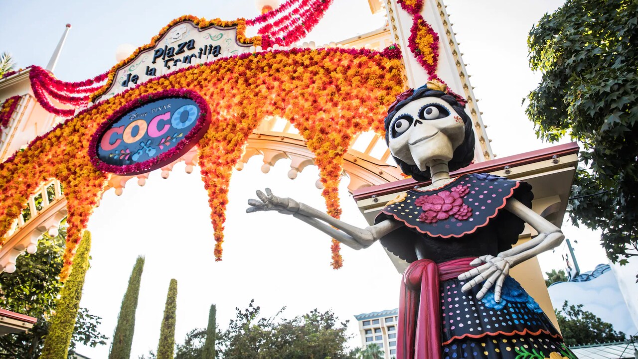 Un arco decorado con flores y letreros que dicen, 'Plaza de la Familia' y 'Disney Pixar Coco'