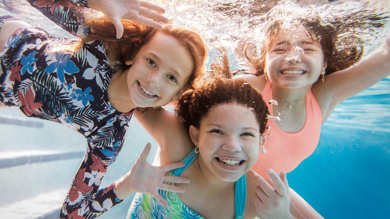 Southern California CityPASS Tres niñas sonríen mientras nadan bajo el agua en una piscina