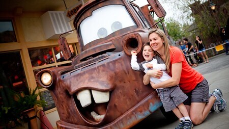 Una mamá arrodillada con su pequeño hijo en brazos, junto a una réplica de la grúa Tow Mater