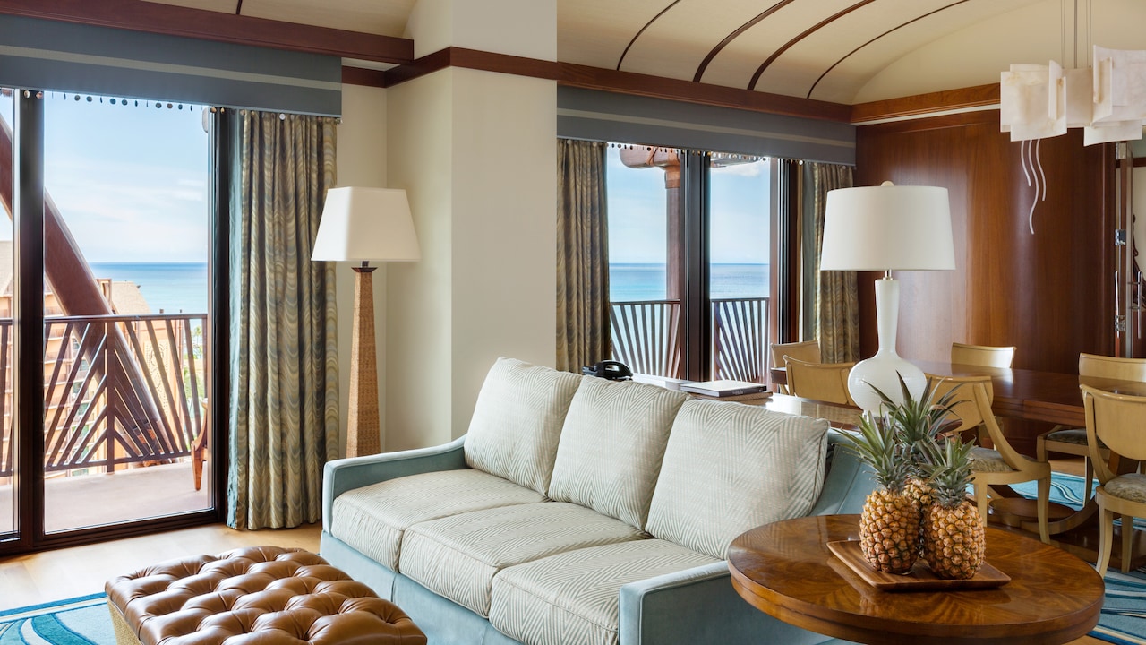 The living area of the Deluxe 1-Bedroom suite has a plush couch and a dining table with chairs