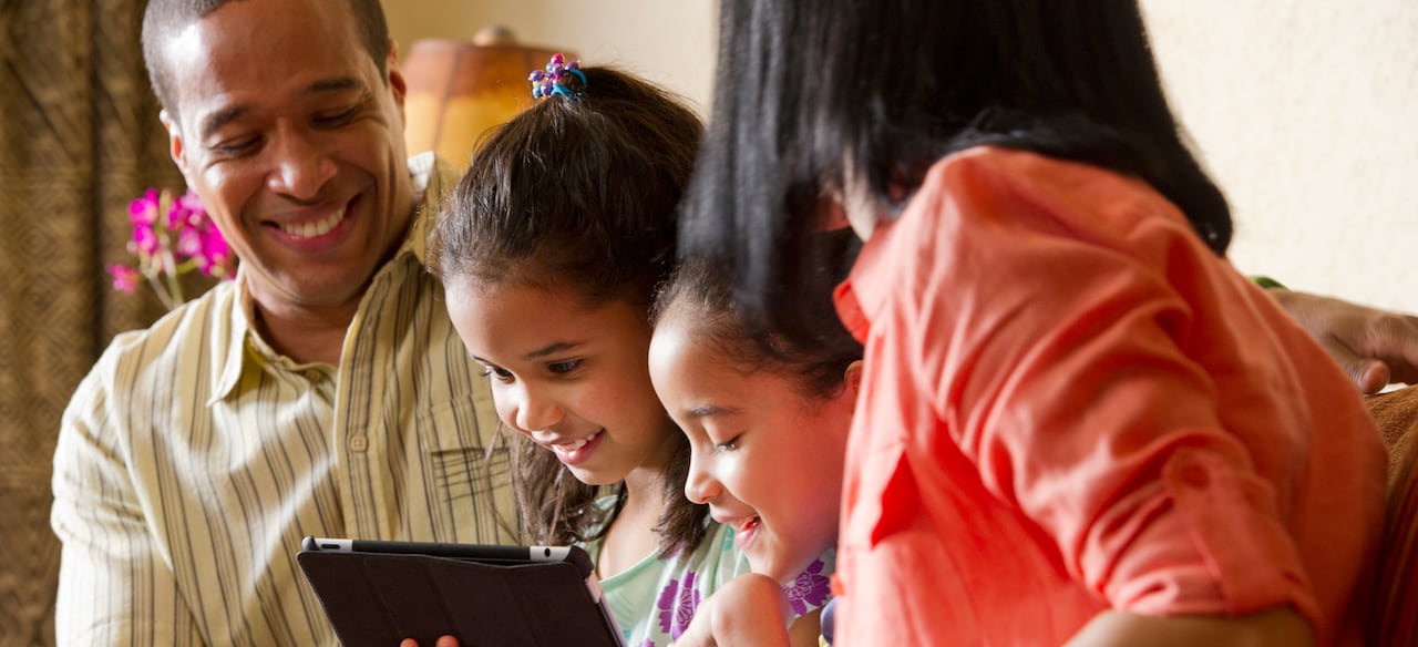 A girl interacts with a mobile tablet as her sister and parents look on